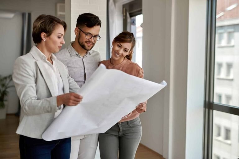 young couple examining blueprints with real estate agent while buying new home
